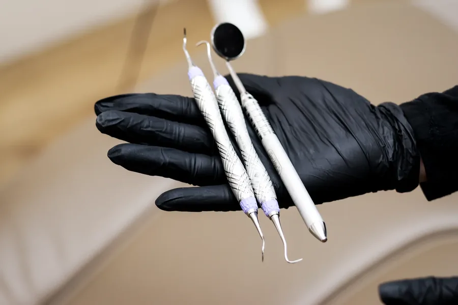Gloved hand holding three sterilized dental hygiene instruments
