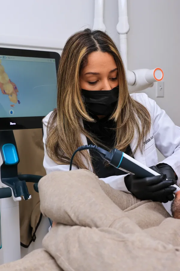 Dentist holding a digital intraoral scanner wand beside the scan on screen
