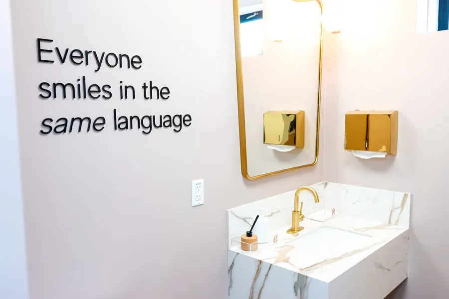 Wall lettering reading Everyone smiles in the same language above the marble vanity