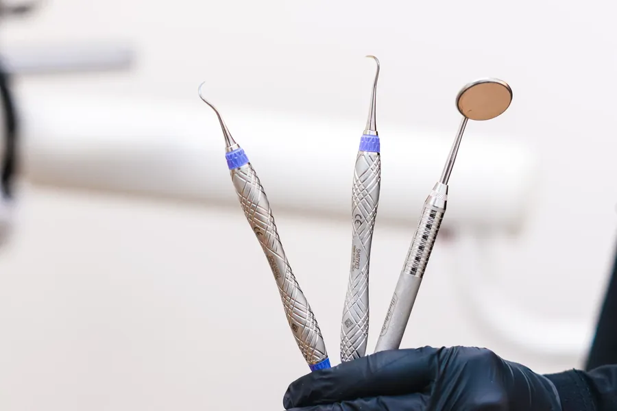 Sterilized dental scaler, explorer and mouth mirror held in a gloved hand