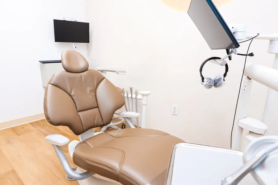 Treatment room with a tan dental chair and an overhead monitor